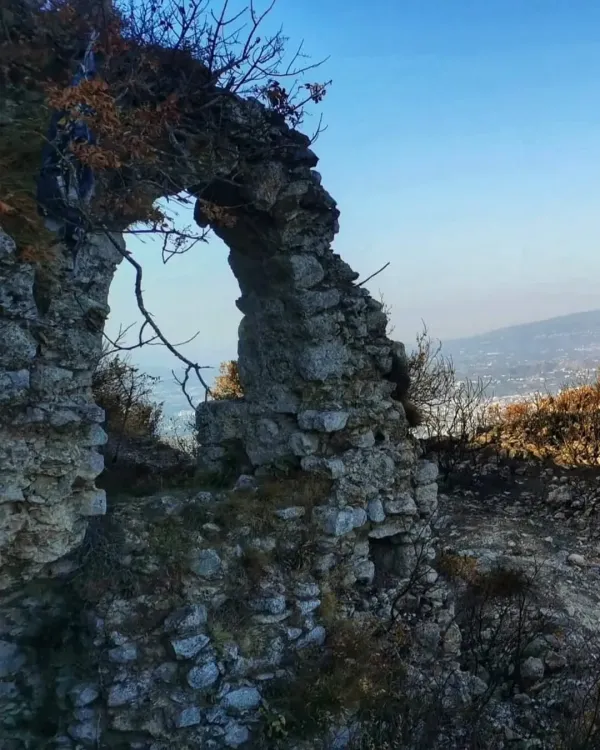 Taş kemer, bitkilerle kaplı, açık gökyüzü ve dağ manzarasıyla çevrili.
