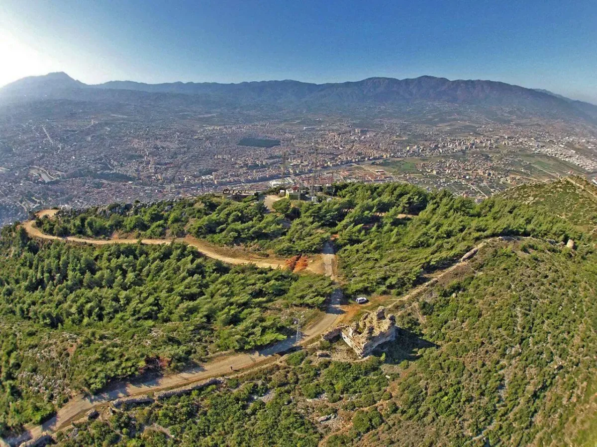 Antakya Kalesi'nin Büyüleyici Manzarası - Yeşil ağaçlarla kaplı bir alan ve şehir manzarası, dağlarla çevrili Yeşil ağaçlarla kaplı bir alan ve şehir manzarası, dağlarla çevrili.