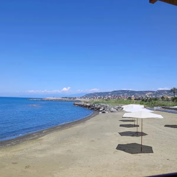 Arsuz plajında beyaz şemsiyeler ve mavi deniz, yaz tatili için ideal bir manzara sunuyor.