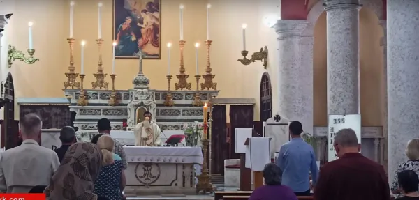 Ayin sırasında sunakta beyaz örtü ve din görevlisi, kalabalık cemaat dua ediyor.