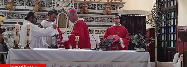 Beyaz örtülü masa, şamdanlar ve kadeh ile üç rahip ayin yapıyor.