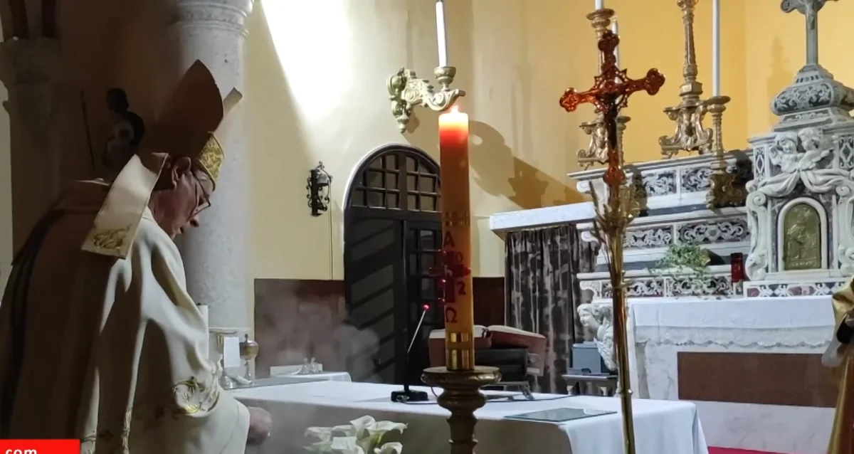 İskenderun Latin Katolik Kilisesi iç mekanında din adamı dua ediyor, dini objeler ve şamdanlar masada.