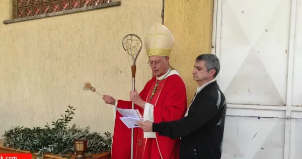 Kırmızı cübbe giymiş din adamı, elinde asa ile tören gerçekleştiriyor.