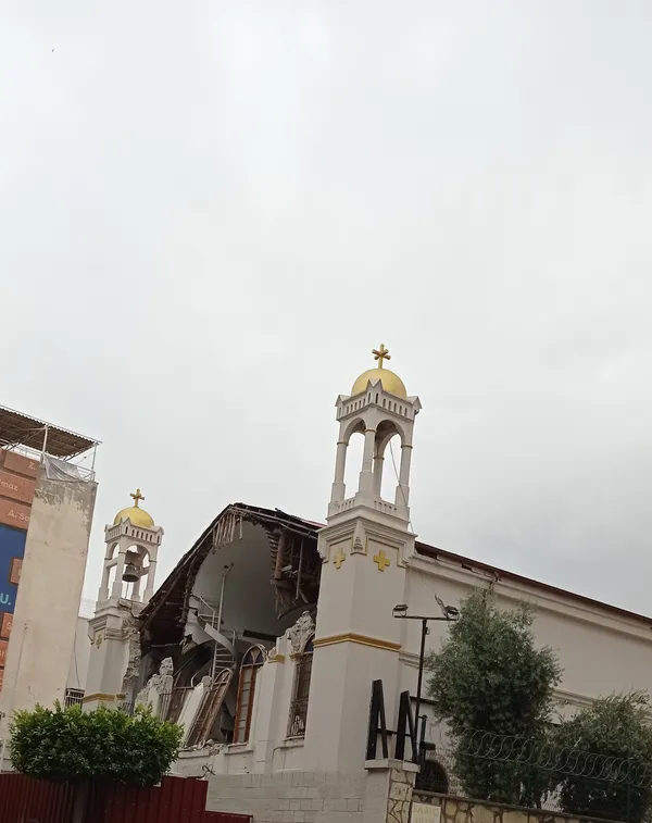 İki altın kubbeli çan kulesi olan tarihi bir kilise, arka planda bulutlu gökyüzüyle.