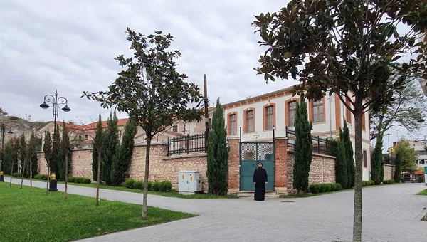 Parkta yürüyüş yolu, ağaçlar ve taş bir bina görünmekte.