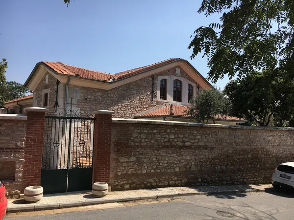 Taş ve tuğla malzemeden yapılmış tarihi bir ortodoks kilisesi, zarif demir kapı ve yeşil bitkilerle çevrili.