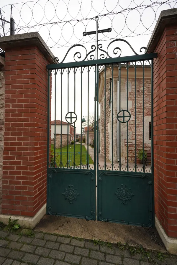 Yeşil demir kapı ve taş yapıyla çevrili düzenlenmiş bahçe görünümü.