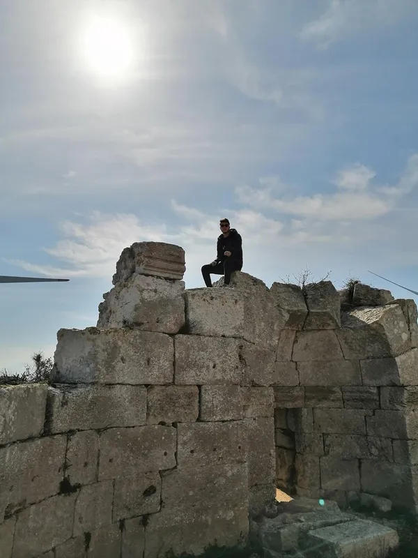 Antik kalıntılar üzerine oturan kişi, güneş ışığında huzurlu bir manzara sunuyor.