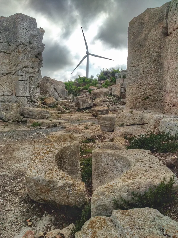Yıkık taş yapılar ve rüzgar türbini ile tarihi ve modern birleşimi.