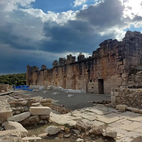 Aşınmış taşlardan oluşan yüksek duvarları olan antik kalıntılar, bulutlu bir havada yeşil ağaçlık alanda yer al
