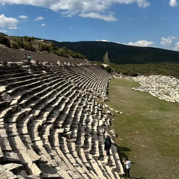 Kibyra antik kentindeki amfi tiyatro kalıntıları, yeşil alan ve dağ manzarası.