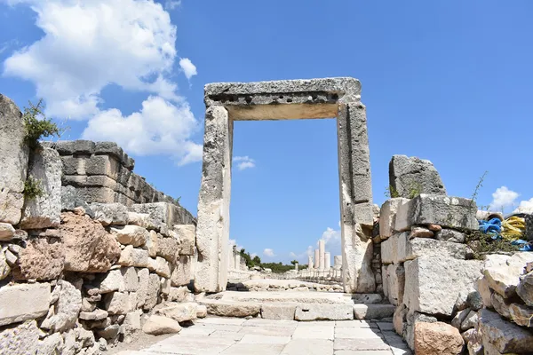 Taş kapı ve yanındaki taş duvarlar, sütunlu yapı silueti arka planda.