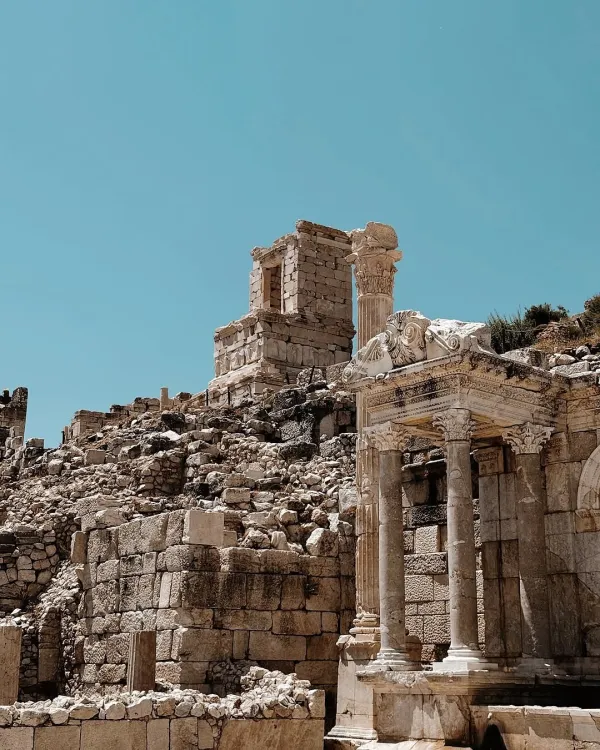 Sagalassos antik kentinde yuvarlak sütunlar ve yıkık taş yapılar, açık mavi gökyüzü altında yer alıyor.