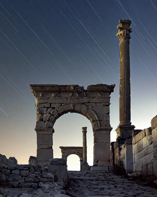 Sütunlu yapılar ve kemerlerle dolu tarihi kalıntılar, yıldız izleriyle süslenmiş gökyüzü altında.