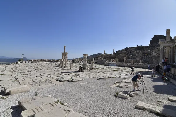 Antik kalıntılar, eski yapılar ve ziyaretçilerin bulunduğu geniş bir açık alan.