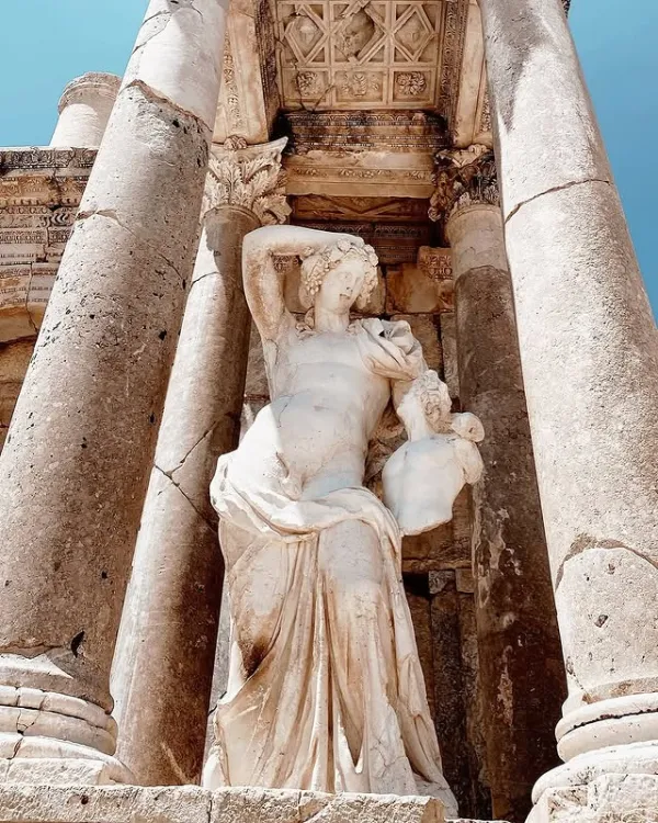 Antik heykel, zarif figür ve büyük taş sütunlar ile tarihi atmosfer sunuyor.