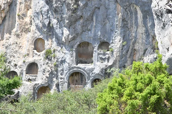 Sarp kayalarda yer alan antik mezar nişleri, doğal yeşillikle çevrili.