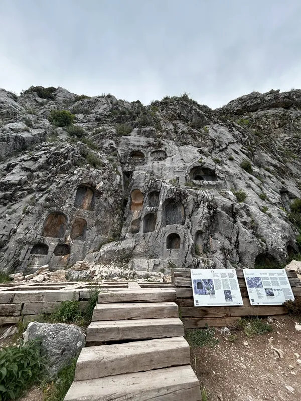 Büyük kayalık yüzeydeki antik mezar nişleri ve ahşap merdiven.