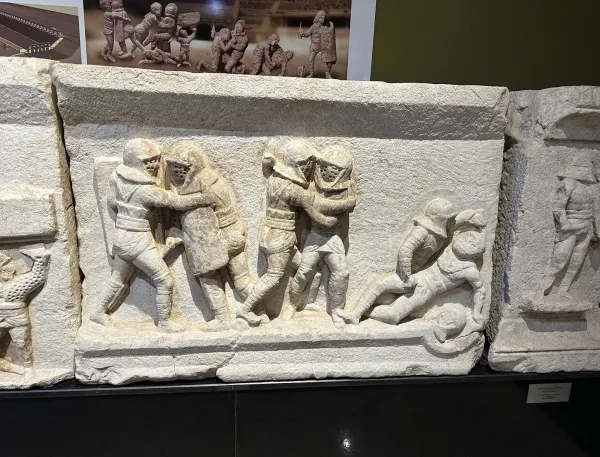 Taş kabartmada antik savaşçıların mücadele sahnesi yer almakta.