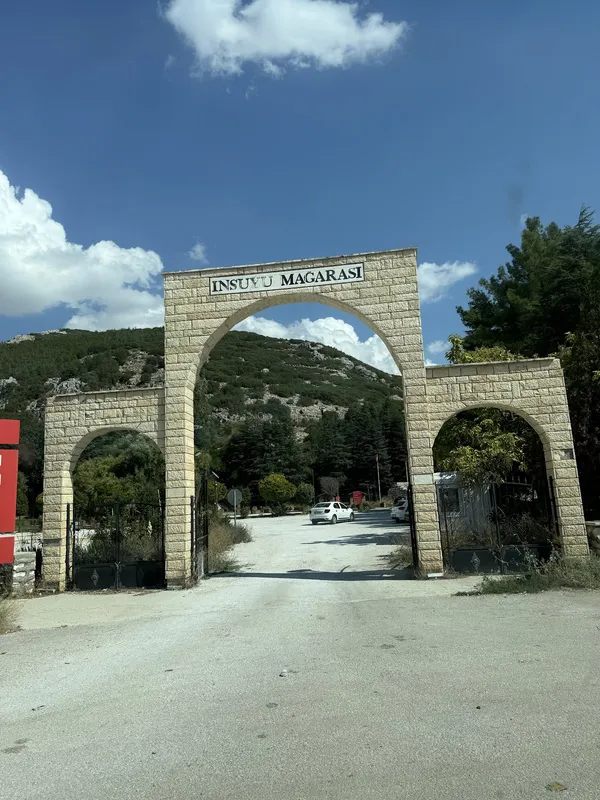 İnsuyu Mağarası'nın taş kemer kapısı, yeşil ağaçlarla çevrili.