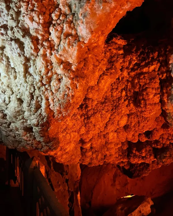 İnsuyu Mağarası'nda sarımsı turuncu ışıkla aydınlatılmış pürüzlü duvarlar ve kristal benzeri yapılar