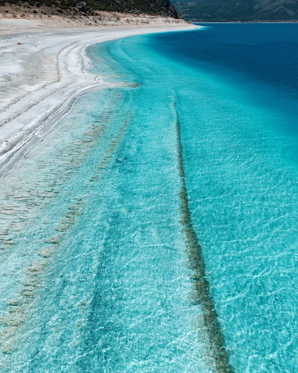 Berrak mavi su ve ince beyaz kum ile huzurlu bir plaj manzarası.