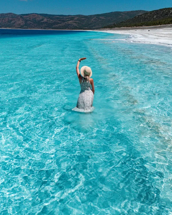 Berrak suda beyaz elbise giymiş bir kadın, kumsalda duruyor.