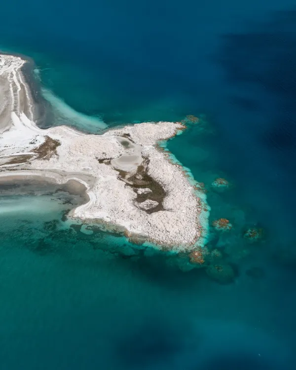 Berrak mavi sularla çevrili yarımada ve beyaz kumsal görünümü