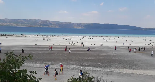 Açık mavi göl ve beyaz tuz alanı ile çevrili dağ manzarası.