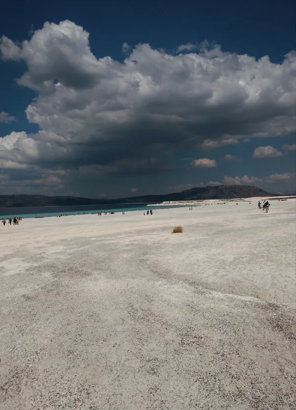 Beyaz tuzlu alan ve mavi göl manzarasında insanlar çeşitli aktiviteler yapıyor.