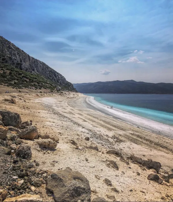 Parlak mavi deniz ve açık renkli kumla kaplı geniş kumsal.