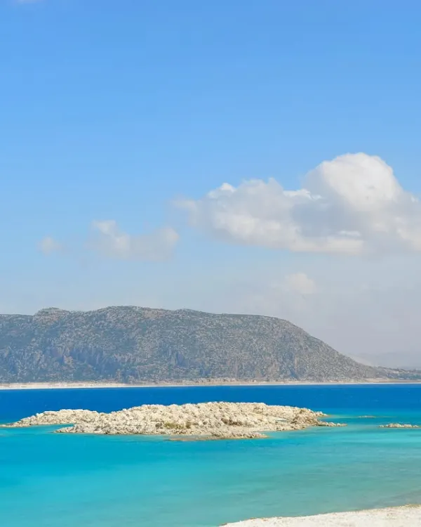 Açık mavi gökyüzü altında turkuaz deniz ve beyaz kumsal manzarası.