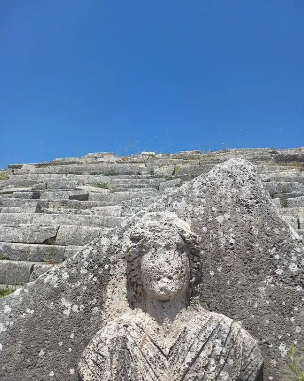 Açık mavi gökyüzü altında antik taş yapı ve heykel görünümü.