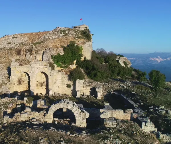 Yüksek tepe üzerindeki antik kalıntılar ve Türk bayrağı, mavi gökyüzüyle çevrili.