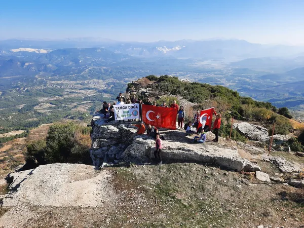 Kremna Antik Kenti'nde grup insan, Türk bayraklarıyla doğa yürüyüşünde.