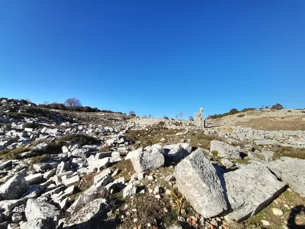 Taşlarla kaplı arazide antik yapı kalıntıları ve heykel görünümü.