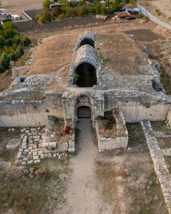 Yıkık taş yapı, üç kemer ve çevresinde yeşil ağaçlar ile doğal peyzaj.