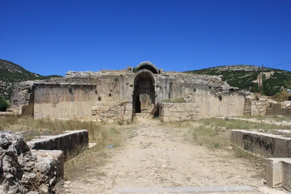 Yüksek mavi gökyüzü altında tarihi taş yapı kalıntısı ve büyük kemer.