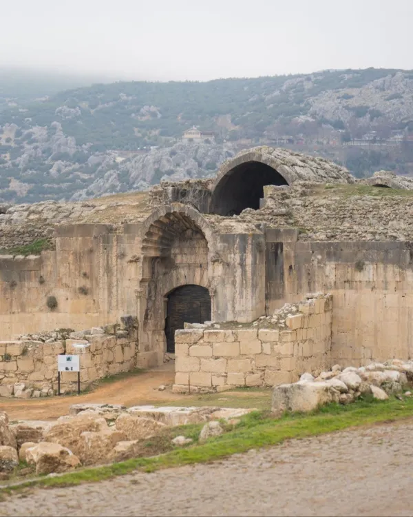 Antik yapının yuvarlak kemerli girişi ve taş duvarları, arka planda sisli dağ manzarasıyla birlikte görülüyor.