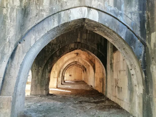 Taş duvarlarla çevrili geniş bir koridor, büyük kemerler ve doğal ışık sızıntılarıyla dolu.