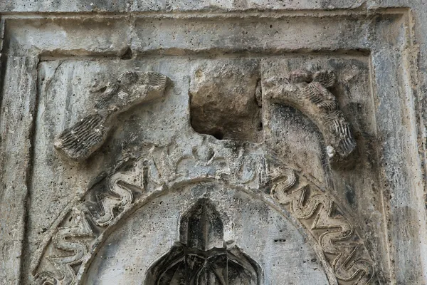 Eski taş yapıda kabartma, kuş figürleri ve dalgalı desenler yer alıyor.