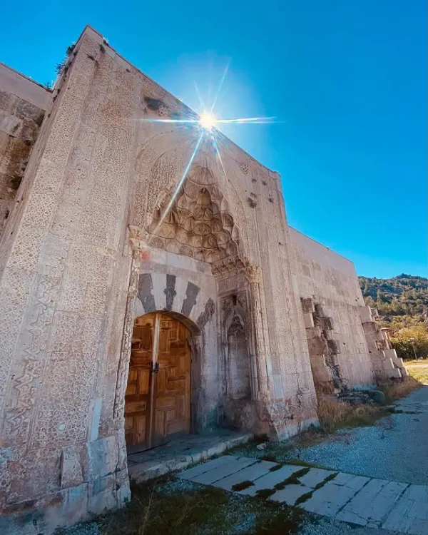 Tarihi yapının etkileyici kapısı, zarif taş işçiliği ve doğal çevresiyle dikkat çekiyor.