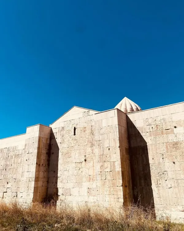 Büyük taş yapının duvarları ve üçgen çatısı açık mavi gökyüzüyle tezat oluşturuyor.