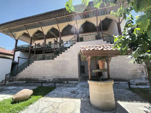 Geleneksel bir yapının avlusunda, balkonlar ve taş işçiliğiyle süslü geniş bir bina yer alıyor.