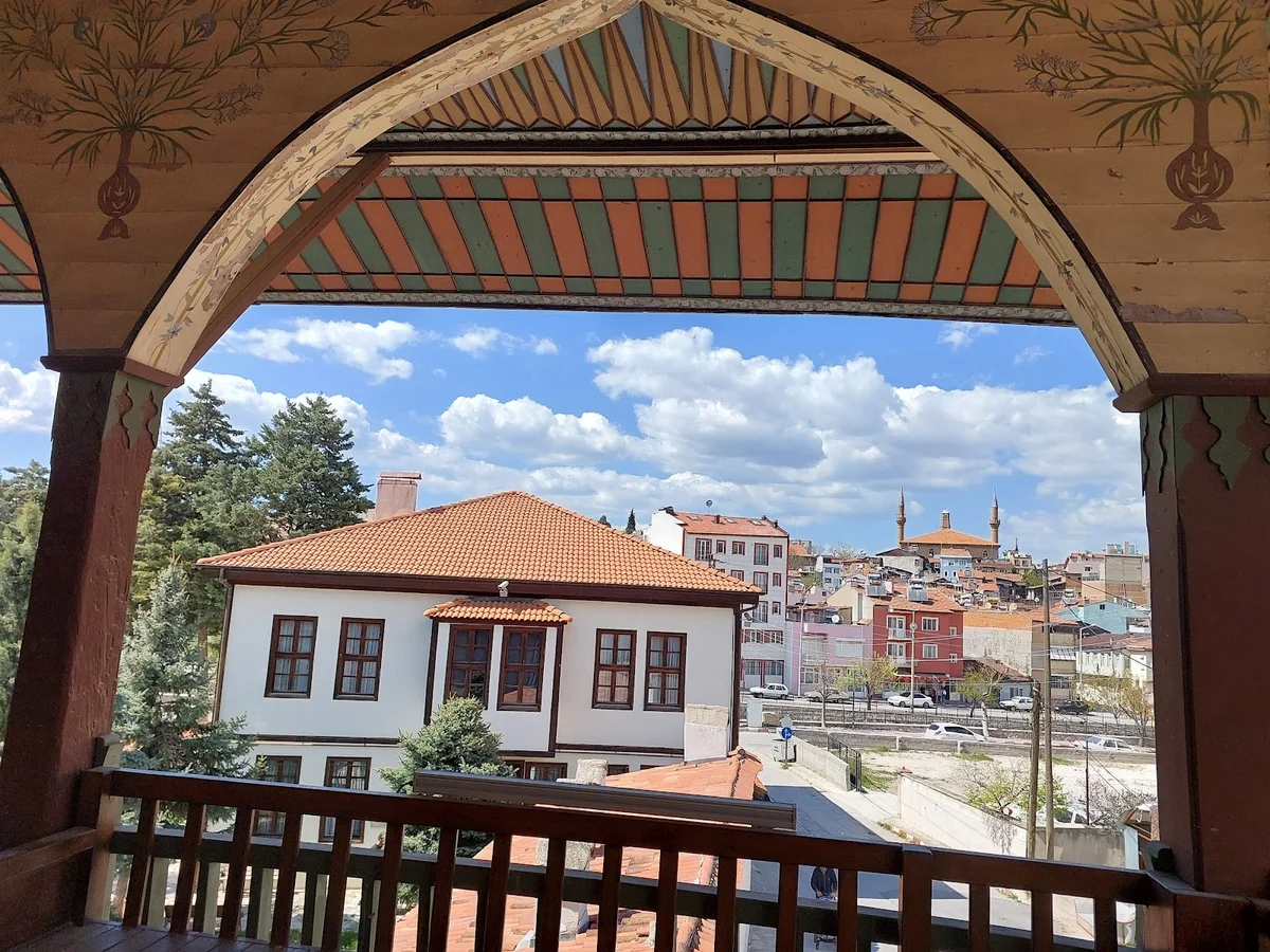 Eşsiz Manzara: Tarihi Bakibey Konağı ve Arka Plandaki Camiler! Beyaz geleneksel ev, turuncu kiremit çatısı ve arka planda camilerle tarihi bir manzara.