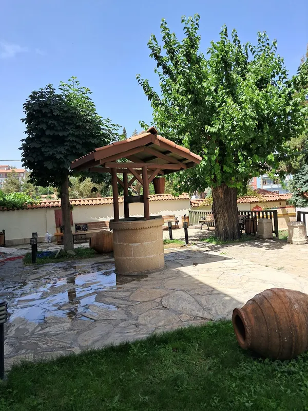 Yeşil ağaçlarla çevrili açık alanda çatılı kuyu ve banklar
