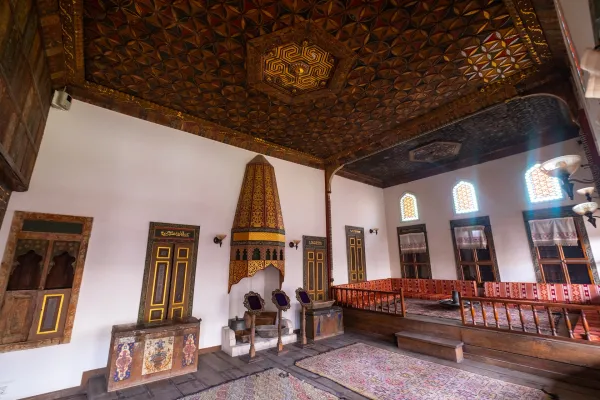 Geleneksel iç mekan, altın detaylı tavan, vitraylı büyük pencereler ve renkli halılarla sıcak bir atmosfer sunuyor.