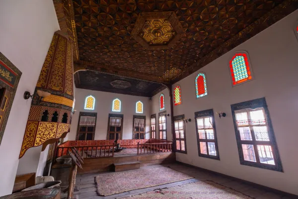 Geleneksel iç mekan, ahşap tavan ve vitraylı pencerelerle aydınlatılıyor.