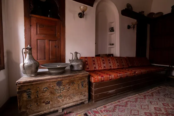 Uzun kanepede kırmızı örtüler, metal sürahiler ve dokuma halı ile sıcak bir oturma odası.