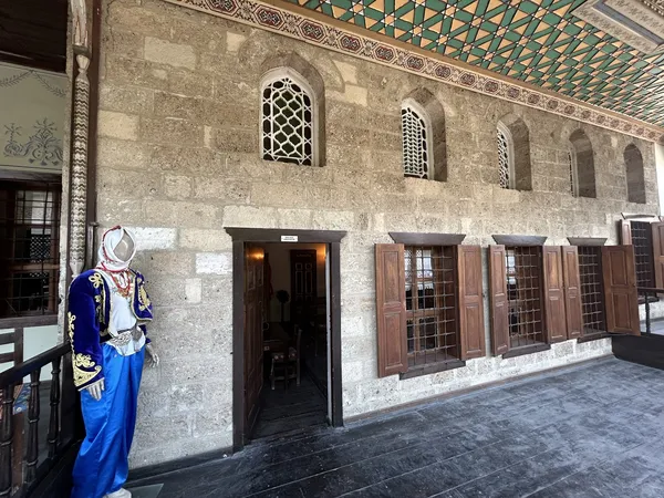 Geleneksel taş duvarlarla inşa edilmiş konağın dış cephesi, işlemeli elbiseler sergileyen manken ile birlikte.